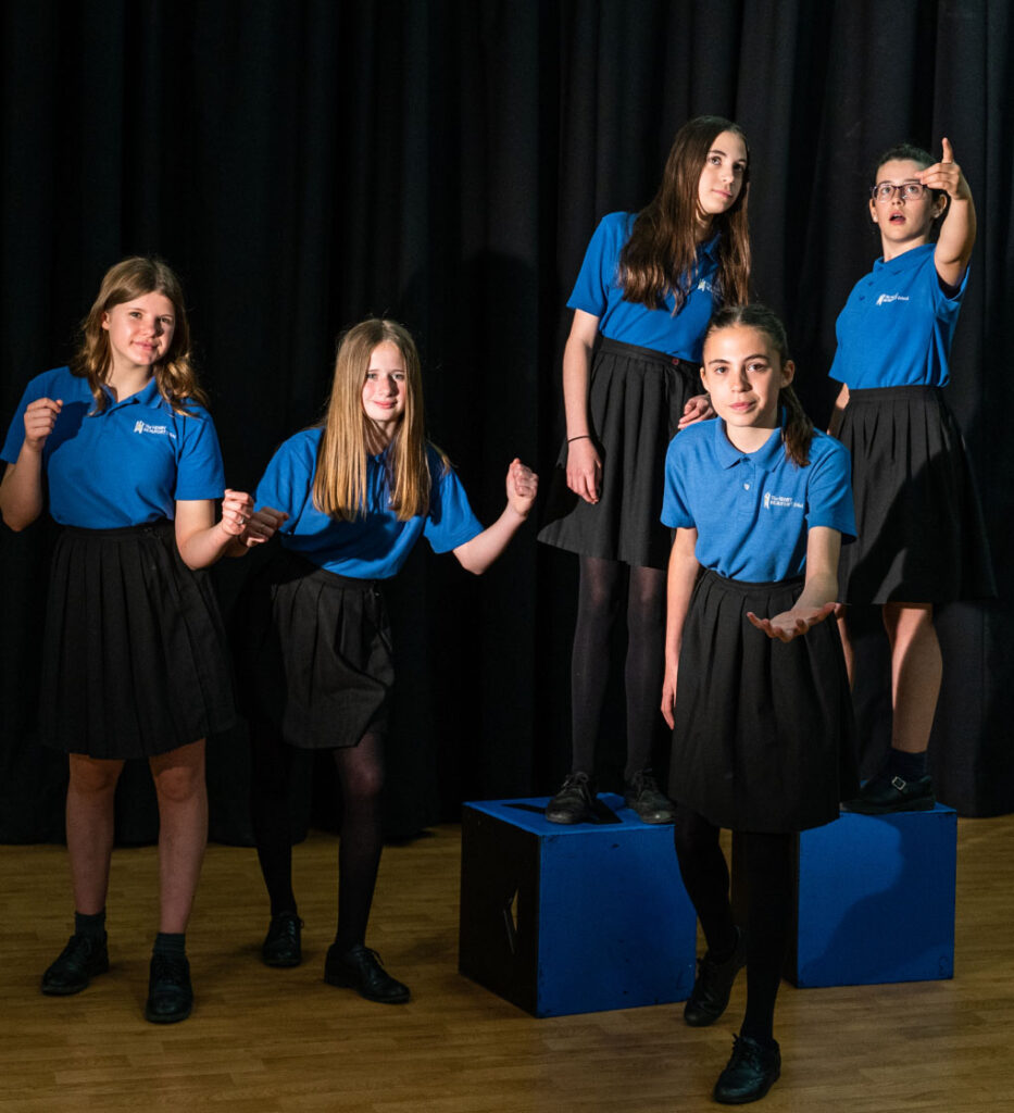Group of students posturing on stage as part of a drama lesson.