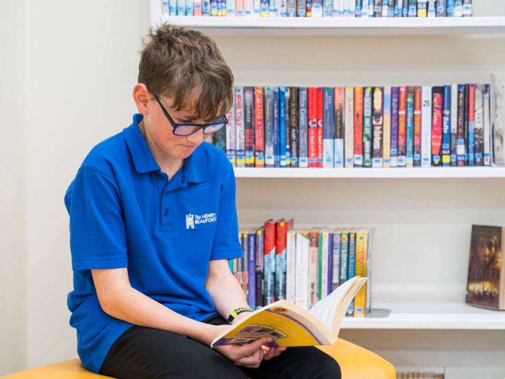 Student looking down towards an open book in the library, reading.